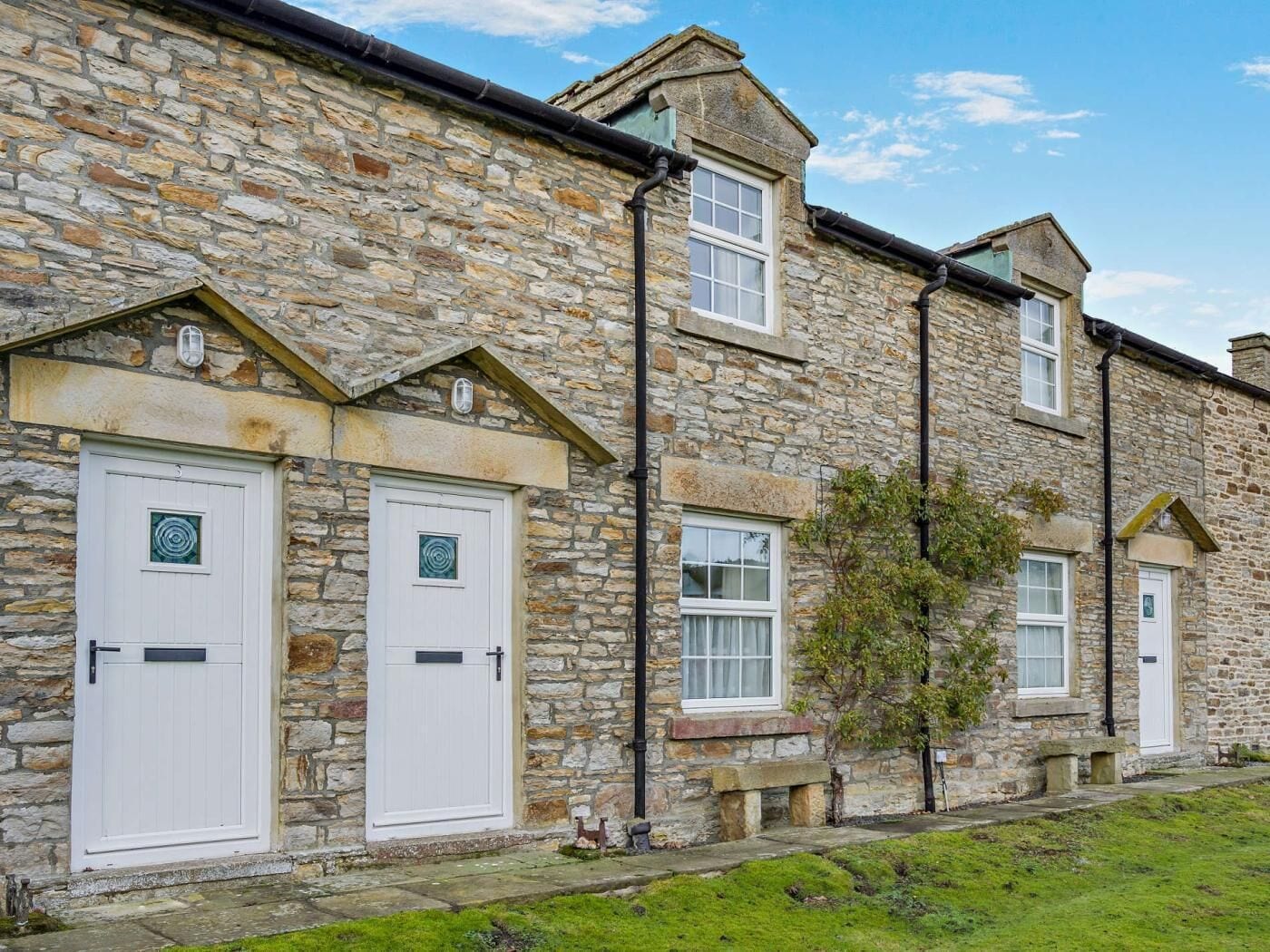 A stone building with two white doors, a bench, and a small tree.