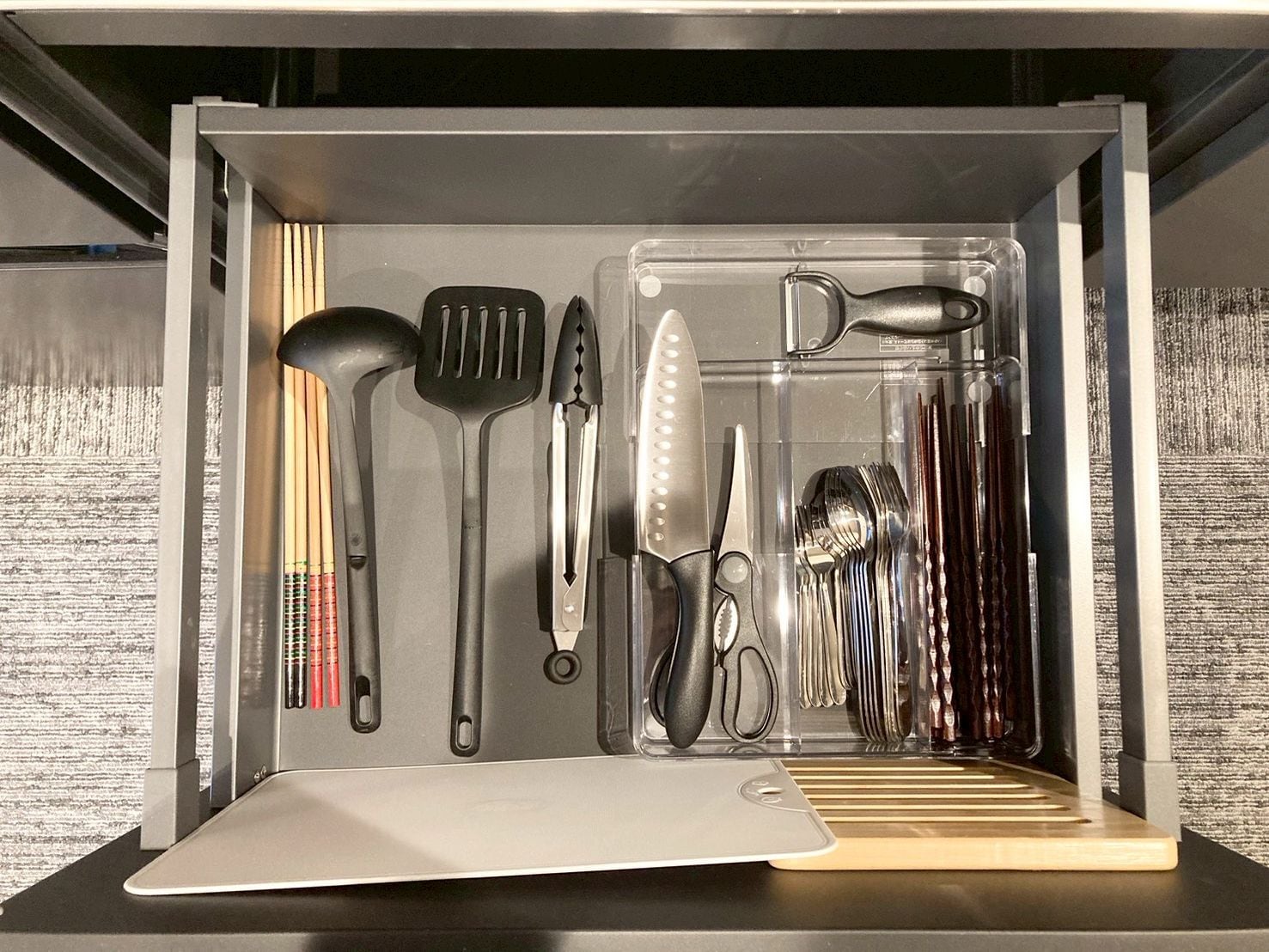 Un cajón de cocina con utensilios, como una espátula, pinzas y un par de tijeras.