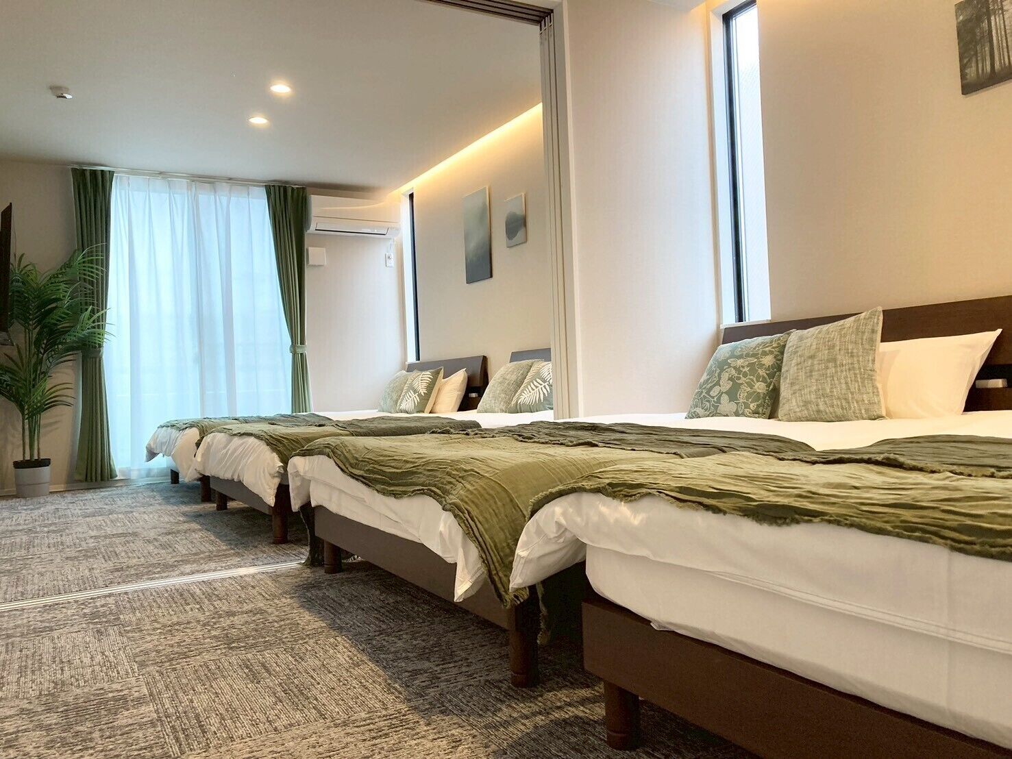 A hotel room with a large bed, a potted plant, and a window with curtains.