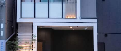 A multi-story building with a garage entrance, a balcony on the upper floor, and a small outdoor area with plants.