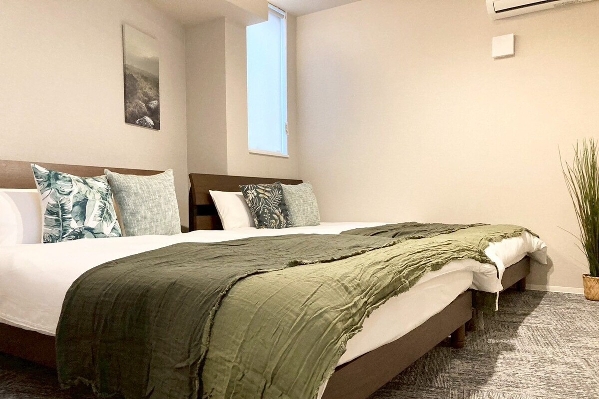 Quarto com cama grande, janela, planta e quadro na parede.