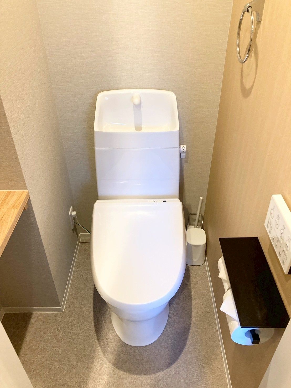 A compact, modern bathroom with a white toilet, a small trash bin, and a toilet paper holder on the wall.
