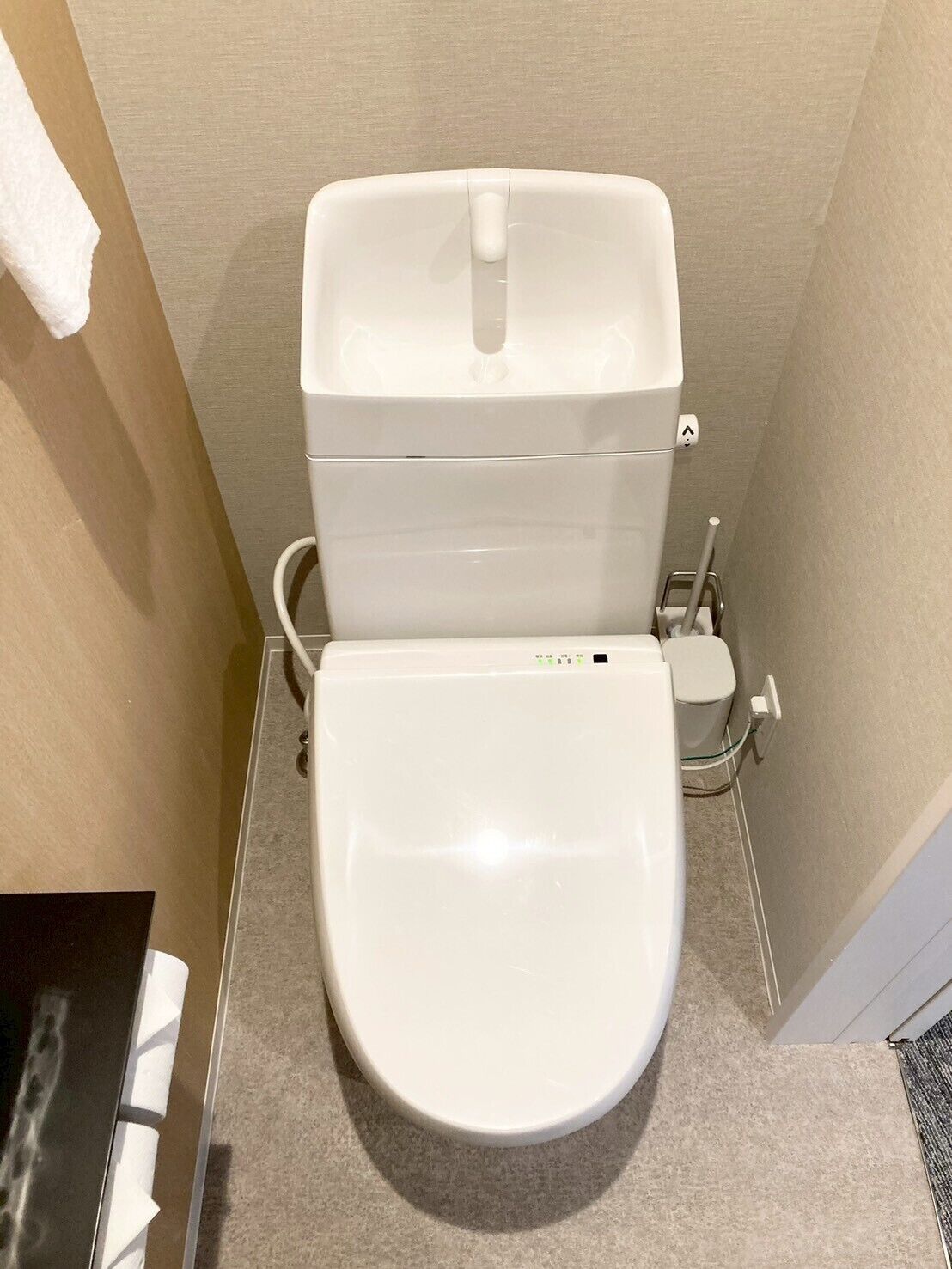 Inodoro blanco con tanque y asiento, un accesorio para bidé y un pequeño cubo de basura.