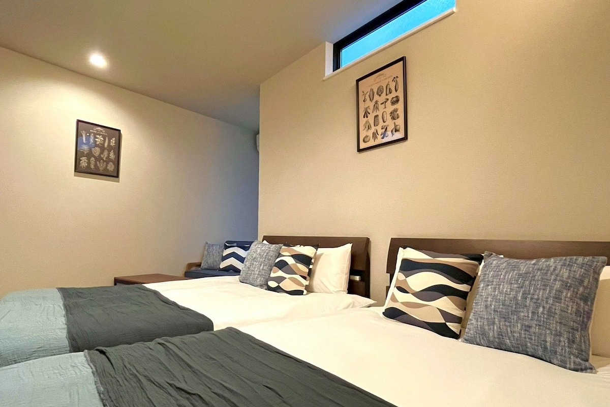 Quarto de hotel com duas camas, uma luminária no teto e um quadro na parede.
