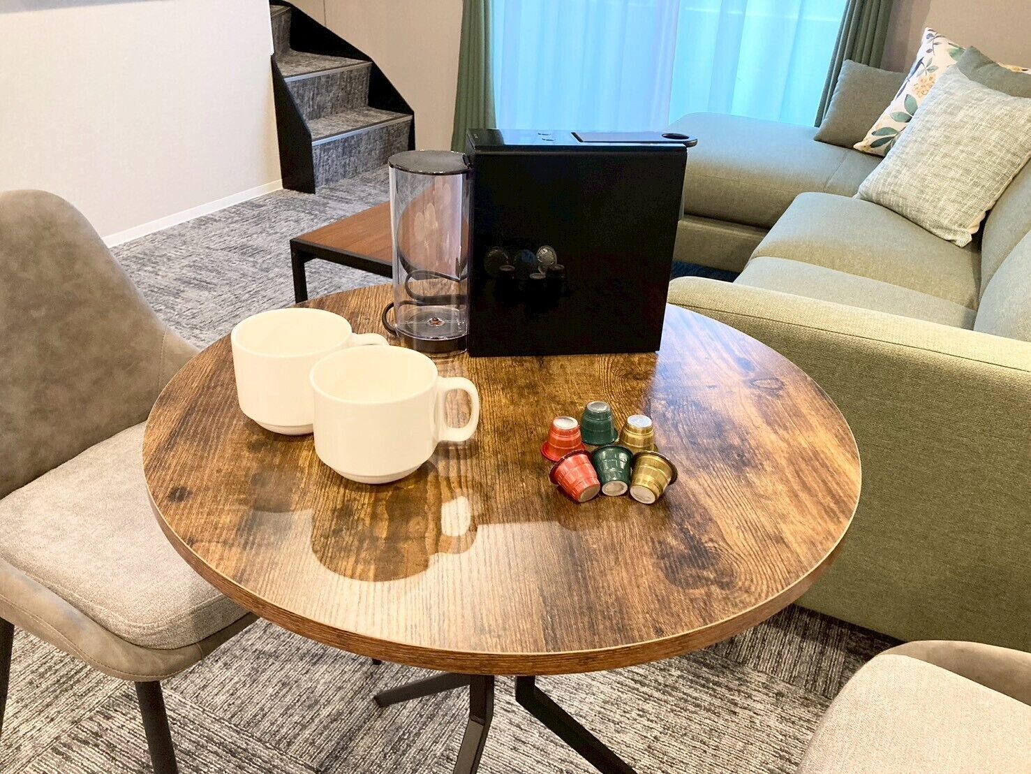 A round wooden table with two white mugs, a glass container, and a black box.