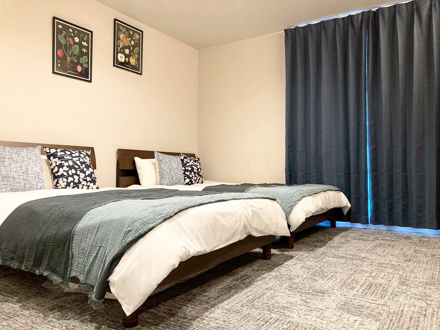 A double bed with a grey blanket, two pillows, a headboard, and a dark curtain.
