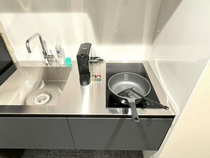 Ett modernt kök med en diskho i rostfritt stål, en inbyggd induktionshäll och en stekspade som ligger på hällen.