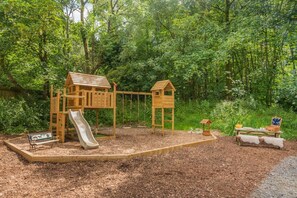 Un parque infantil con tobogán y estructuras para escalar, rodeado de árboles.