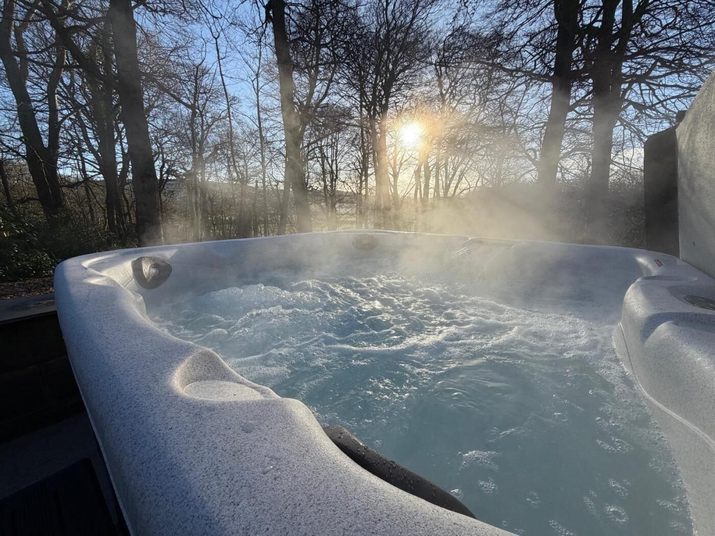 A hot tub surrounded by trees with steam rising from the water.