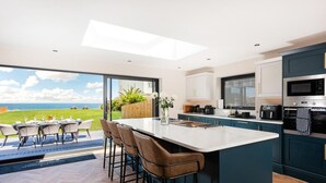 A modern kitchen with a large island, bar stools, and a view of the ocean. - 4 Bed in Sheringham (oc-96433) (Sheringham)