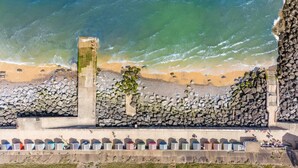 A coastal view with a stone wall, beach, and a row of colorful containers. - 4 Bed in Sheringham (oc-96433) (Sheringham)