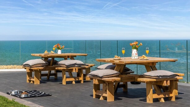 Outdoor wooden tables with cushions, a glass railing, and a view of the sea. - 4 Bed in Sheringham (oc-96433) (Sheringham)