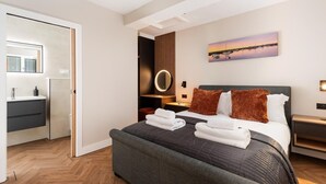 A modern hotel room with a bed, bedside tables, a mirror, and a painting on the wall. - 4 Bed in Sheringham (oc-96433) (Sheringham)