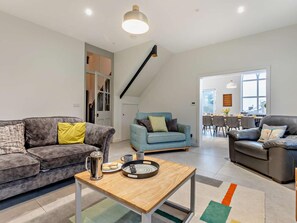 A modern living room with a sofa, a coffee table, and a blue armchair. There is a staircase with a black railing leading to an upper level. - 6 Bed in Prestatyn (oc-96435) (Prestatyn)
