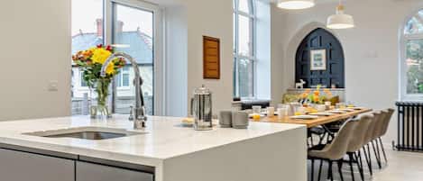 Una cocina moderna con una isla grande, una zona de comedor con mesa y sillas, y ventanas amplias que dejan entrar luz natural.