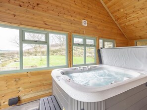 A wooden cabin with a hot tub, large windows, and a view of the countryside.
