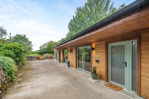 A row of wooden cabins with large sliding doors, a paved driveway, and potted plants.