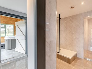 A modern bathroom with a bathtub, a shower, and a glass door leading to a kitchen area.