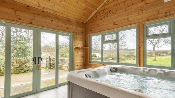 Une cabane en bois dotée d’un bain à remous, de grandes fenêtres et d’un mur en pierre à l’extérieur.
