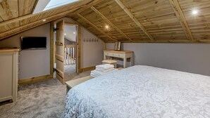 Une chambre avec un plafond en pente, un puits de lumière, un lit, un bureau et un téléviseur.