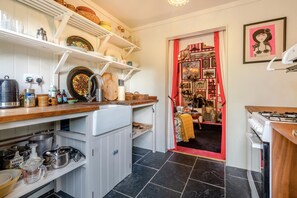 A kitchen with white cabinets, a stove, and various kitchen utensils. There is a doorway leading to a dining area with a red curtain. - 1 Bed in Eye- (oc-34390) (Stoke Ash)