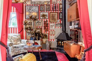 A cozy living room with a floral sofa, a wooden table with a vase and fruit, and a red and white striped wall with framed pictures. - 1 Bed in Eye- (oc-34390) (Stoke Ash)