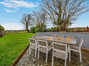 An outdoor patio with a table and chairs, surrounded by a grassy lawn and trees. - 4 Bed in Tyn-y-gongl (oc-96455) (Marianglas)