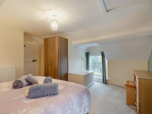 Ein Schlafzimmer mit einem Bett, einem Kleiderschrank, einem Schreibtisch und einem Fenster mit Vorhängen.