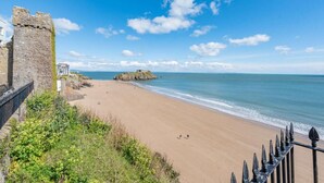 A beach with a stone wall and a rocky outcrop in the distance. - 2 Bed in Tenby (oc-fb232) (Tenby)
