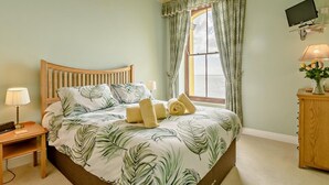 A bedroom with a bed, a nightstand, a lamp, a TV, and a window with curtains. - 2 Bed in Tenby (oc-fb232) (Tenby)