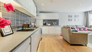 Een moderne keuken met witte kastjes, een houten vloer en een grijze bank in de woonkamer.