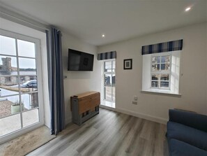 A room with a large window, a flat-screen TV mounted on the wall, a wooden cabinet, and a blue sofa.