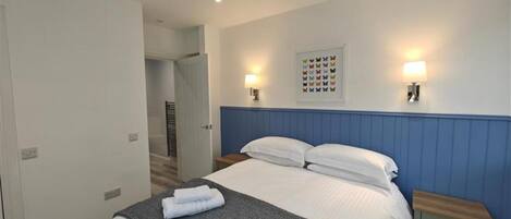 Ein Hotelzimmer mit einem Bett, zwei Nachttischen, einer Wandleuchte und einer Tür zu einem weiteren Raum.
