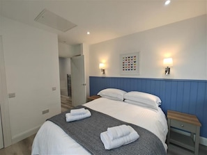 A hotel room with a bed, two bedside tables, a wall-mounted light fixture, and a door leading to another room.