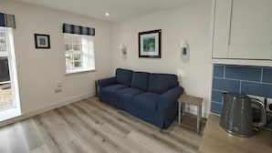 A modern living room with a sofa, a small table, a kettle, and a window with curtains. - 1 Bed in Isle Of Arran (oc-96463) (Machrie)
