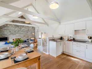 A modern kitchen with white cabinets, a stone wall, and a dining area with a wooden table set for four. - 2 Bed in Cardigan (oc-41684) (Tresaith)