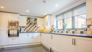 A modern kitchen with white cabinetry, a built-in oven, and a window with blinds. - 5 Bed in Bridport (oc-bigov) (Charmouth)