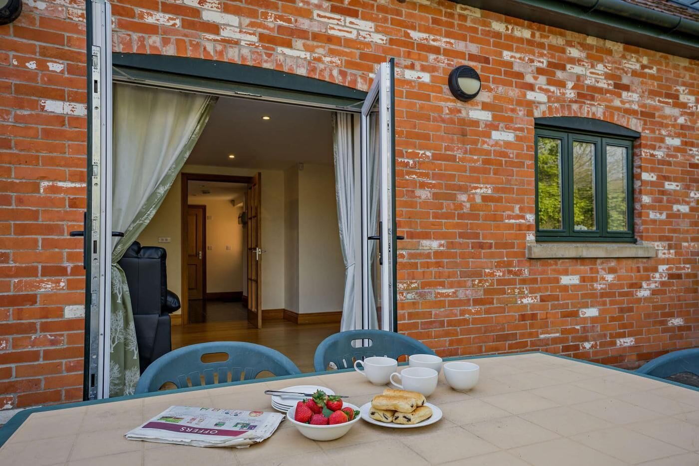 A brick building with a dining area featuring a table with plates of food, cups, and a newspaper.