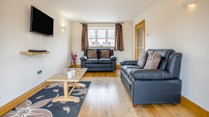 Ein Wohnzimmer mit einer Couch, einem Couchtisch, einem an der Wand montierten Fernseher und einem Fenster mit Vorhängen.