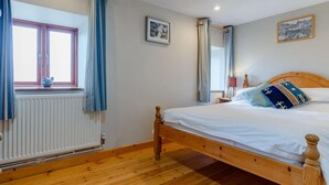 Un dormitorio con una cama de madera, una ventana con cortinas, un radiador y un cuadro colgado en la pared.