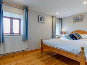 Ein Schlafzimmer mit einem hölzernen Bett, einem fenster mit Vorhängen, einem Heizkörper und einem an der Wand hängenden Bild.