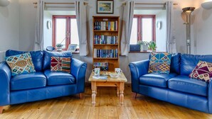 Una sala de estar con dos sofás de cuero azul, una mesa de centro de madera, una estantería y una tabla de surf colgada en la pared.
