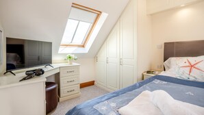Ein Schlafzimmer mit Schreibtisch, Bett, Dachfenster und Kleiderschrank.