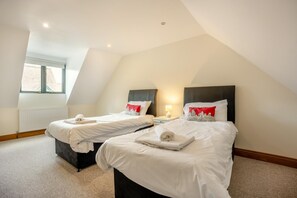 A hotel room with two beds, a window, a radiator, and a nightstand with a lamp. - 2 Bed in Bridport (oc-blueh) (Charmouth)