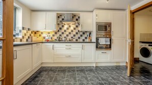 Uma cozinha moderna com armários brancos, painel de azulejos, forno embutido e máquina de lavar.