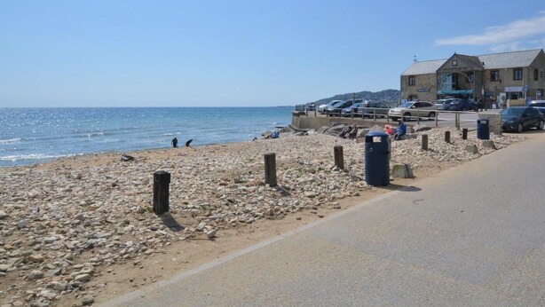 Uma praia com uma estrada, um edifício com um letreiro e carros estacionados.