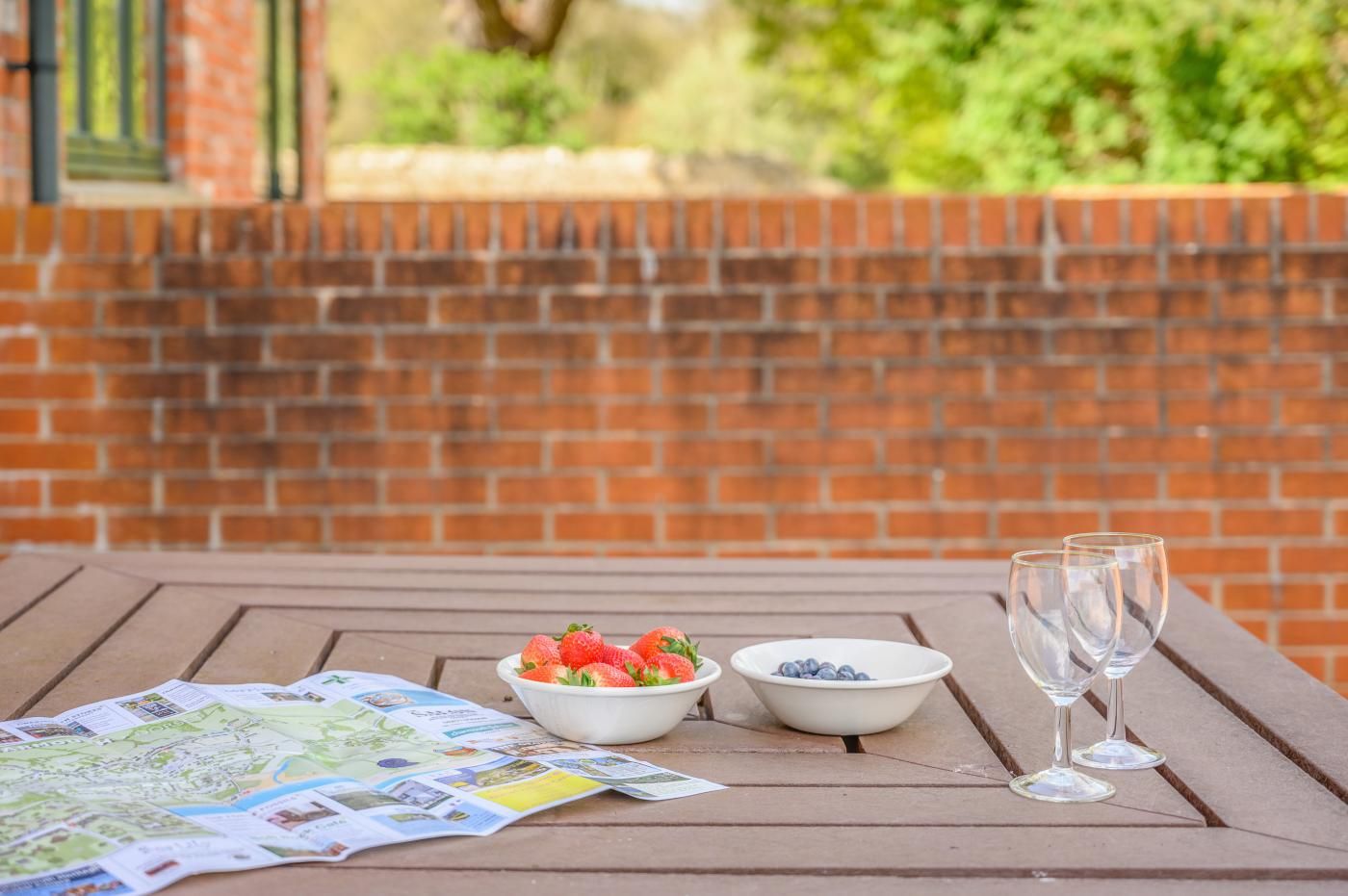 A picnic table with a map, two bowls of fruit, and two empty wine glasses.