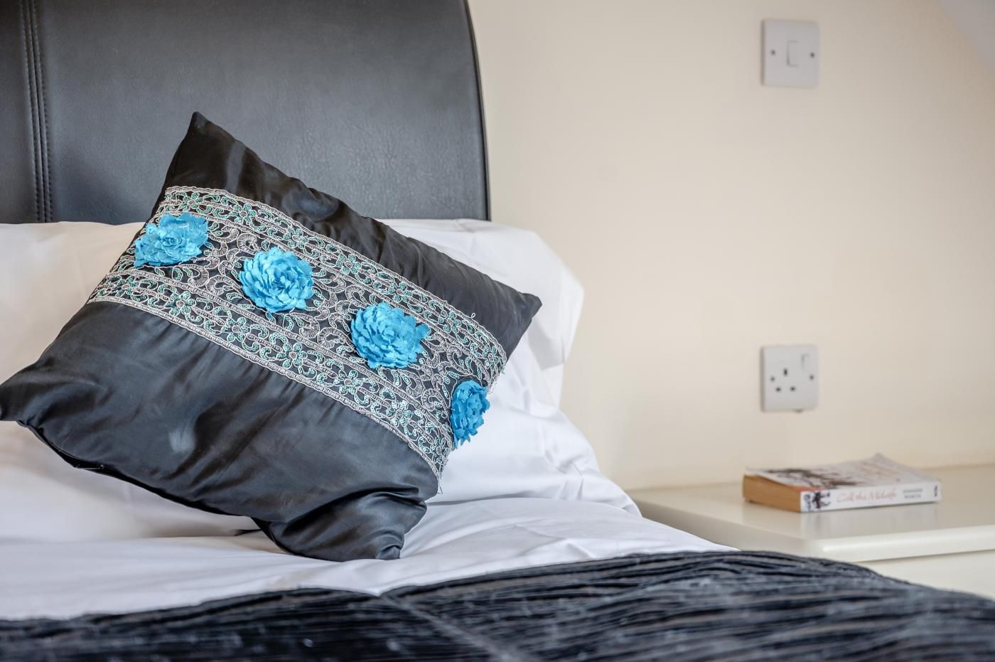 Ein Bett mit einem schwarzen Kopfschild, einer weißen Bettdecke und einem Kopfkissen mit blauem Blumenmuster.