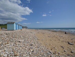 A pebbled beach with a row of light blue beach huts and a clear sky. - 4 Bed in Bridport (oc-shrea) (Charmouth)