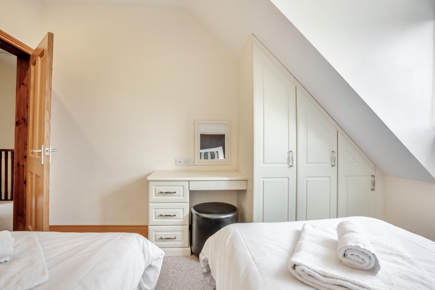 A bedroom with two beds, a desk, a trash bin, and a wardrobe.